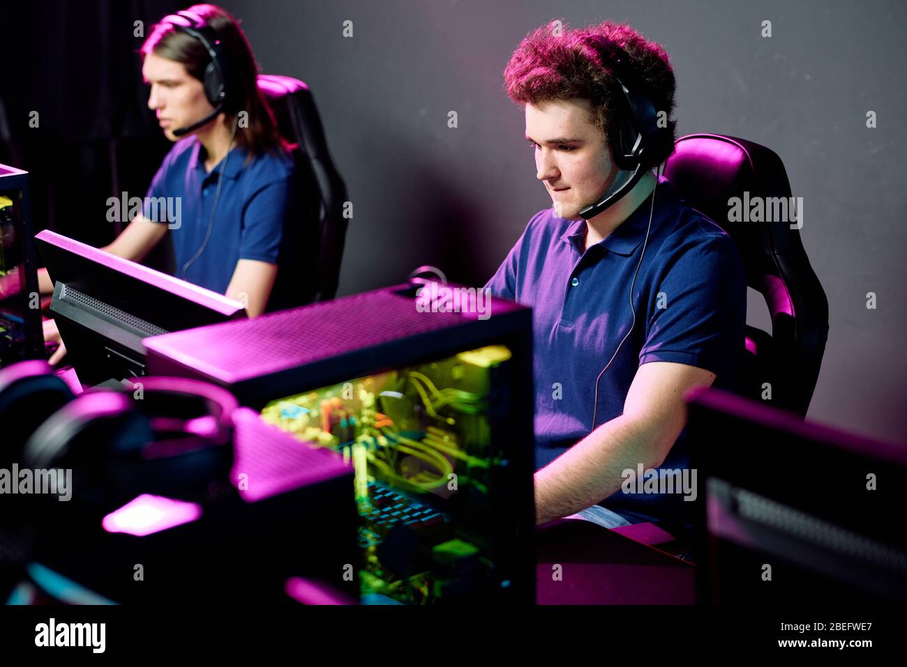 Rangée de jeunes joueurs e-sport concentrés dans des casques avec microphones assis devant des ordinateurs Banque D'Images