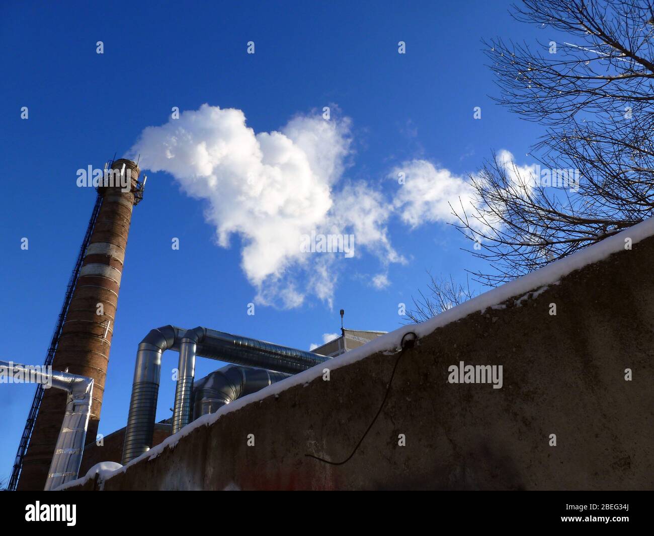 Les tuyaux d'une ancienne usine jettent des nuages de fumée blanche toxique dans le ciel polluant l'atmosphère. Smog urbain provenant de la fumée des chaudières. Fumée blanche d'une cheminée contre un ciel bleu clair. Banque D'Images