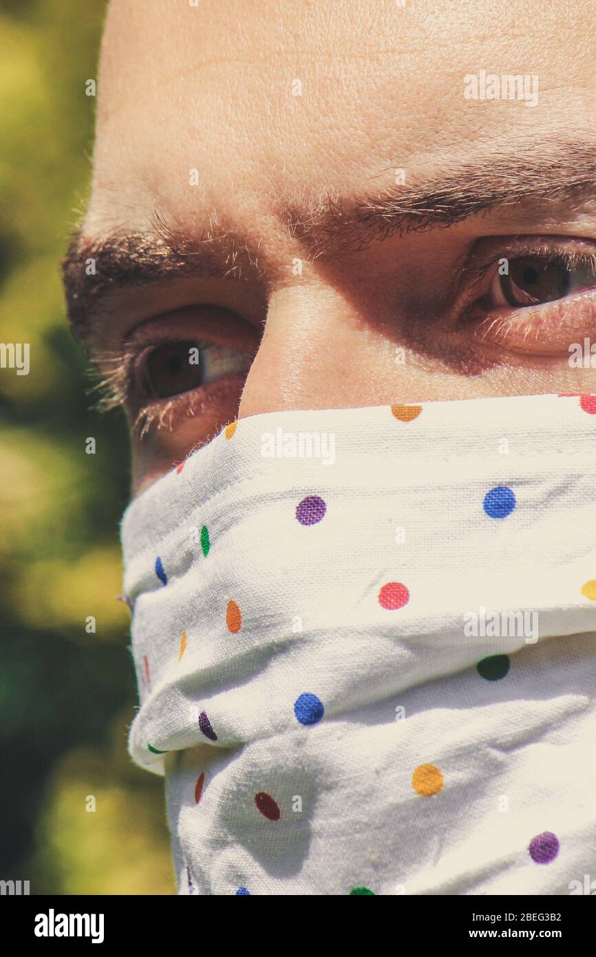 Jeune homme blanc avec un masque fait main en tissu pendant la pandémie de coronavirus. Coronavirus, éclosion de COVID-19. Concept de protection antivirus. Arrière-plan flou. Détail visage et yeux. Banque D'Images