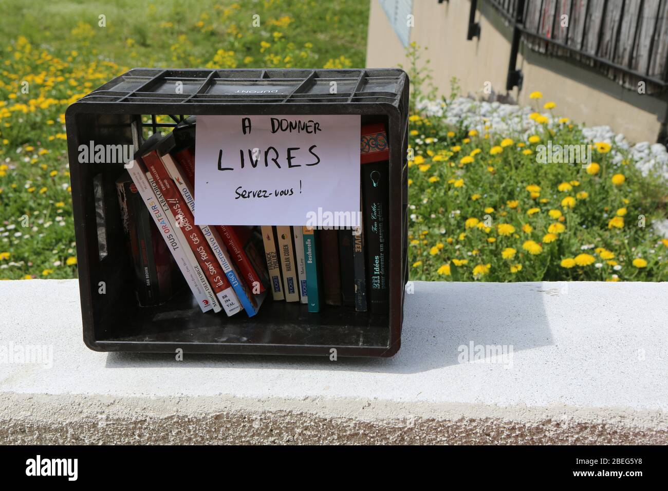 Caisse en plastique noire sur un muret comprant des livres à donner. Saint-Gervais-les-bains. Haute-Savoie. France. Banque D'Images