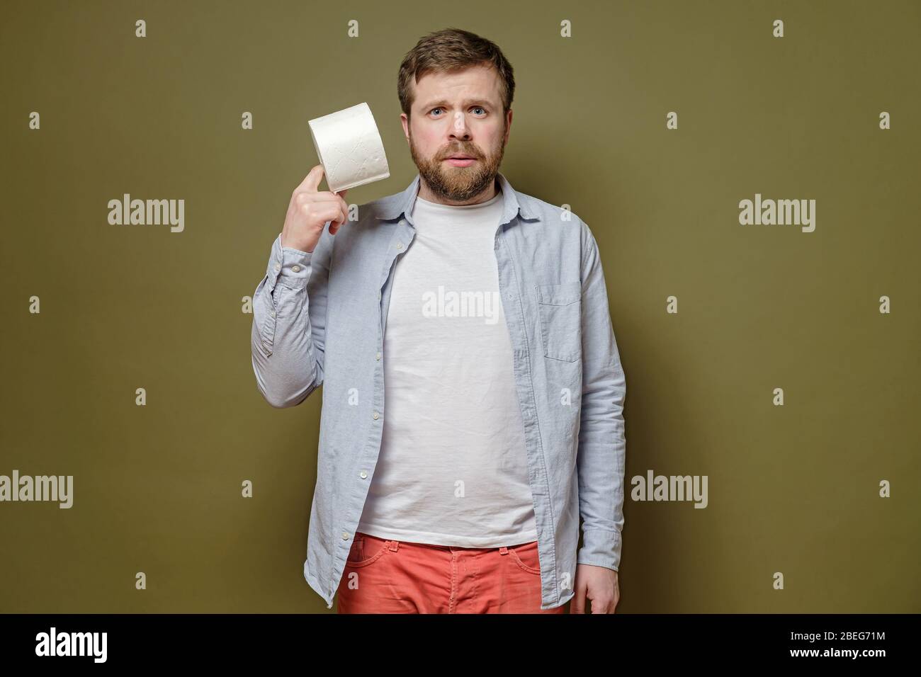 L'homme alarmé tient dans les mains un rouleau de papier toilette, sur un fond vert. Concept de paranoïa infligé avec une épidémie de virus. Banque D'Images