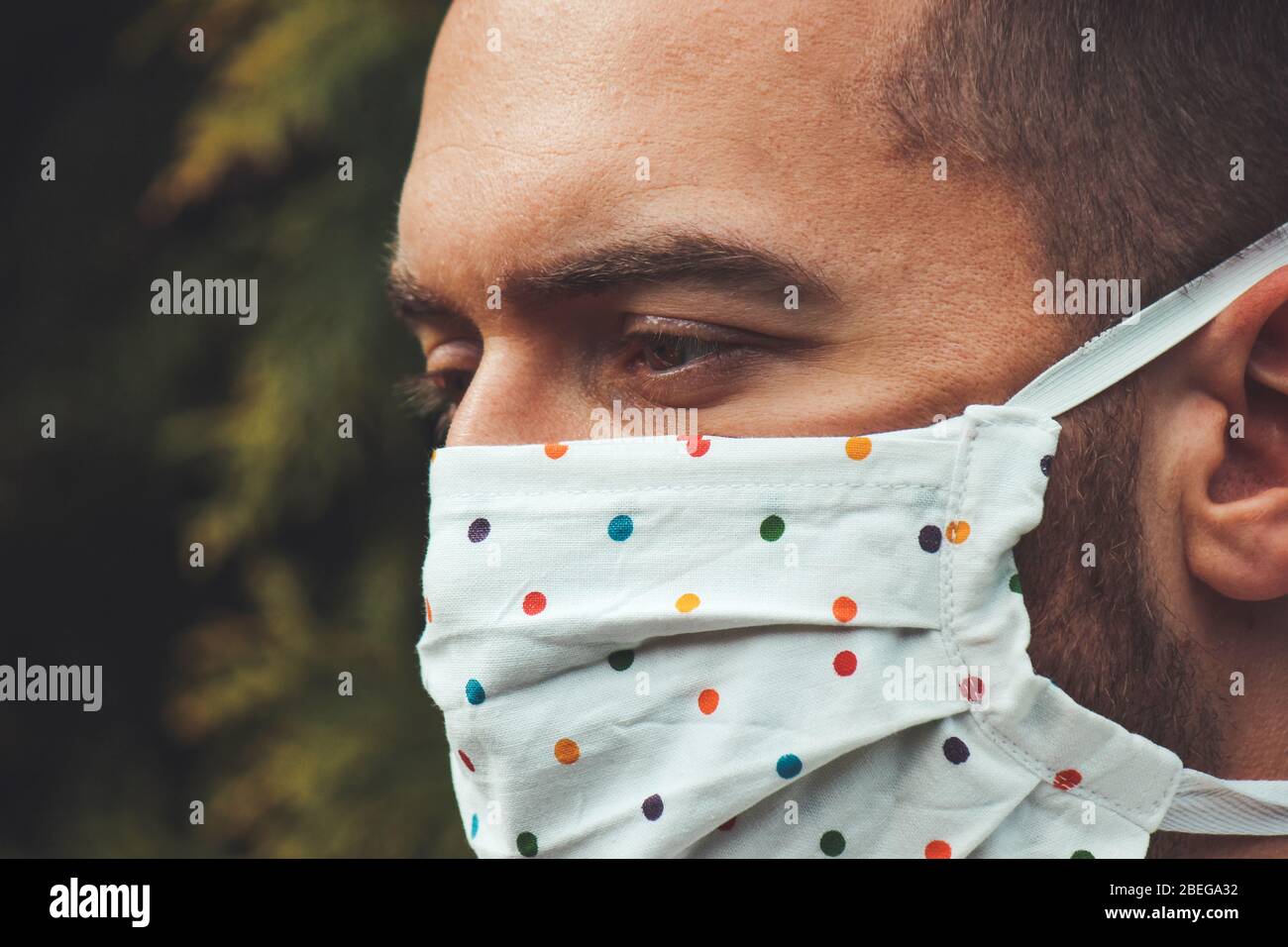 Jeune homme blanc avec un masque fait main en tissu pendant la pandémie de coronavirus. Coronavirus, éclosion de COVID-19. Concept de protection antivirus. Arrière-plan flou. Détail visage et yeux. Banque D'Images