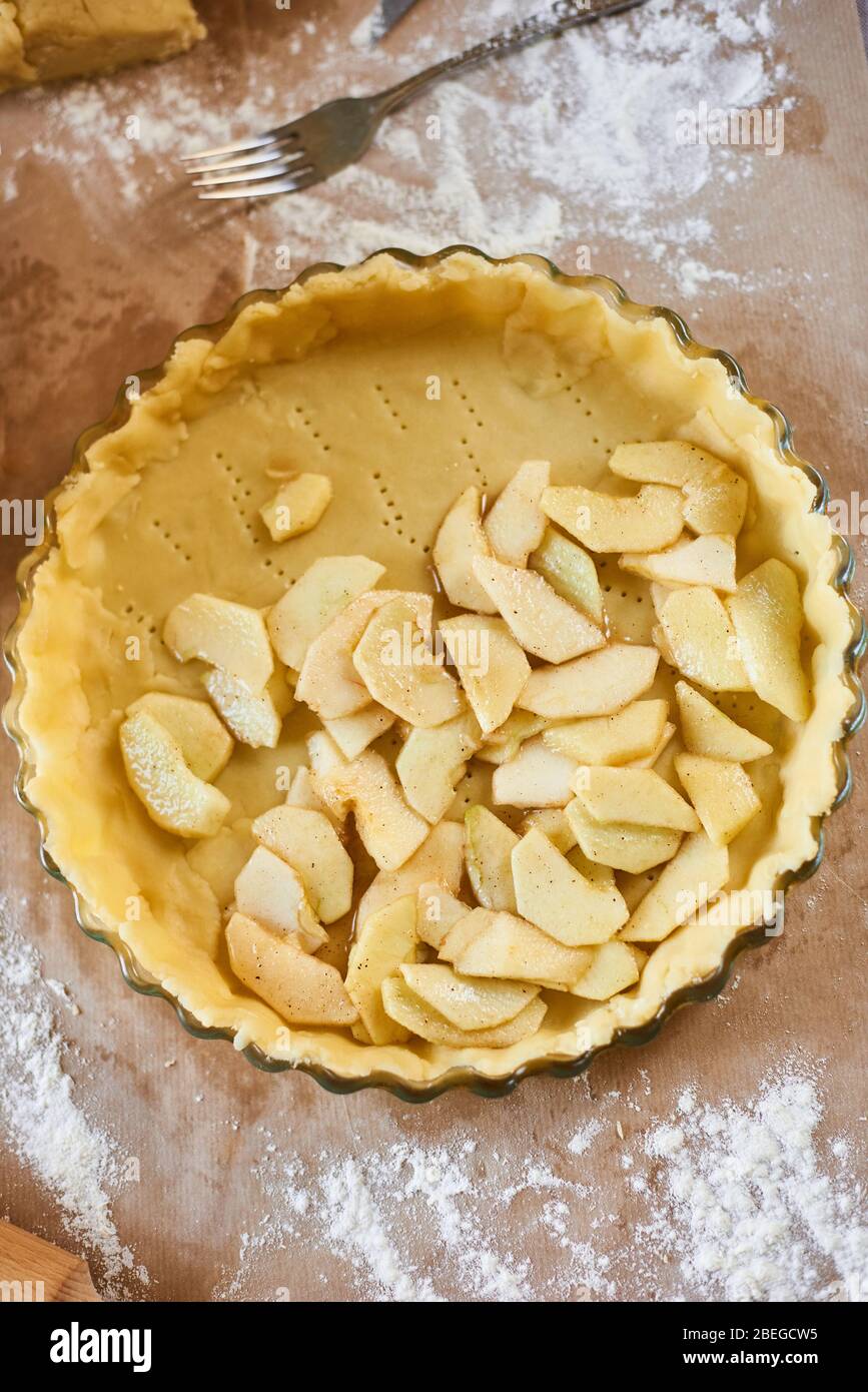 femme ajoute des pommes tranchés à la tarte aux pommes. Femme mains travaillant une pâte à tarte dans un plateau, sur une table de cuisine, entourée d'ingrédients de tarte à la citrouille. Tradition Banque D'Images