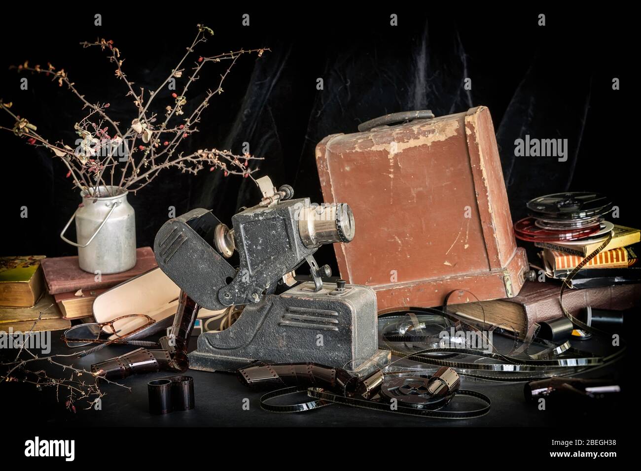 Ancien projecteur vintage pour la visualisation de bandes filmées sur fond de boîte de conditionnement en bois, bobines avec bande de film, piles de vieux livres et fleurs séchées Banque D'Images