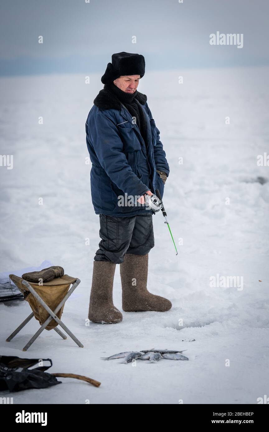 Lac Baikal, Sibérie, Russie - 05 mars 2020 : pêche sur glace d'hiver. Un pêcheur pêche sur des flèches près de tentes et de voitures sur le lac Baikal en mars d Banque D'Images Lac Baikal, Sibérie, Russie - 05 mars 2020 : pêche sur glace d'hiver. Un pêcheur pêche sur des flèches près de tentes et de voitures sur le lac Baikal en mars d Banque D'Images