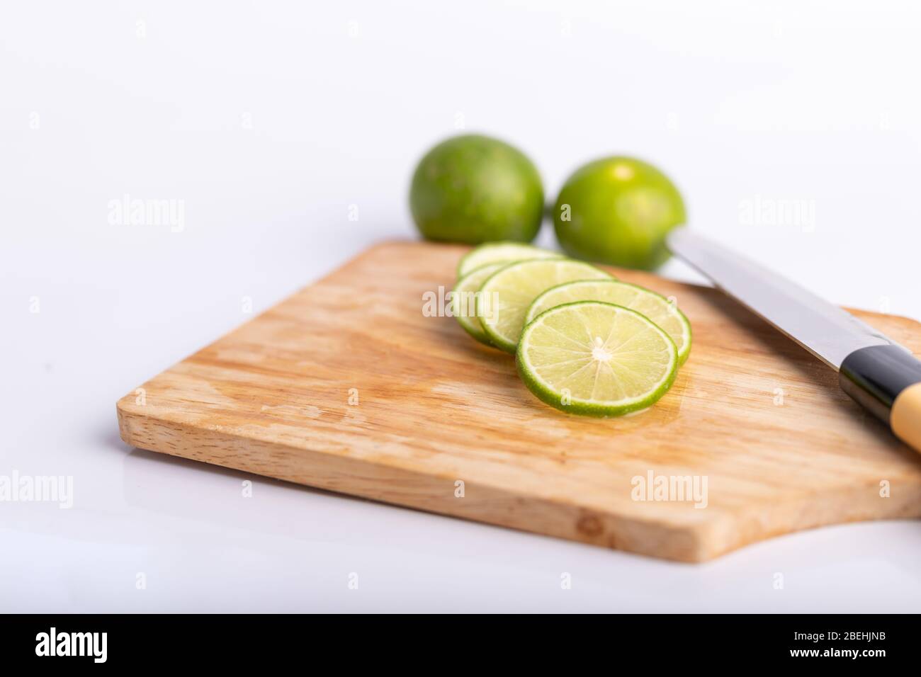 Close up des tranches de lime vert et de graines avec un couteau place sur planche de bois dans une cuisine sur fond blanc. Le citron est un genre de fruit. Le résultat je Banque D'Images