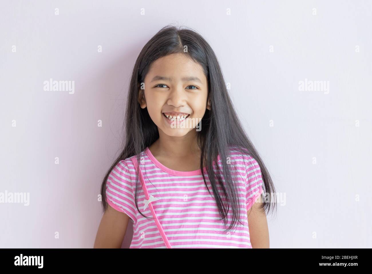 Petite fille asiatique souriante aux couleurs vives. Les enfants portent des robes blanches croisées roses et de longs cheveux noirs. L'enfant regarde vers l'avant et sourit avec plaisir. Portraits Banque D'Images