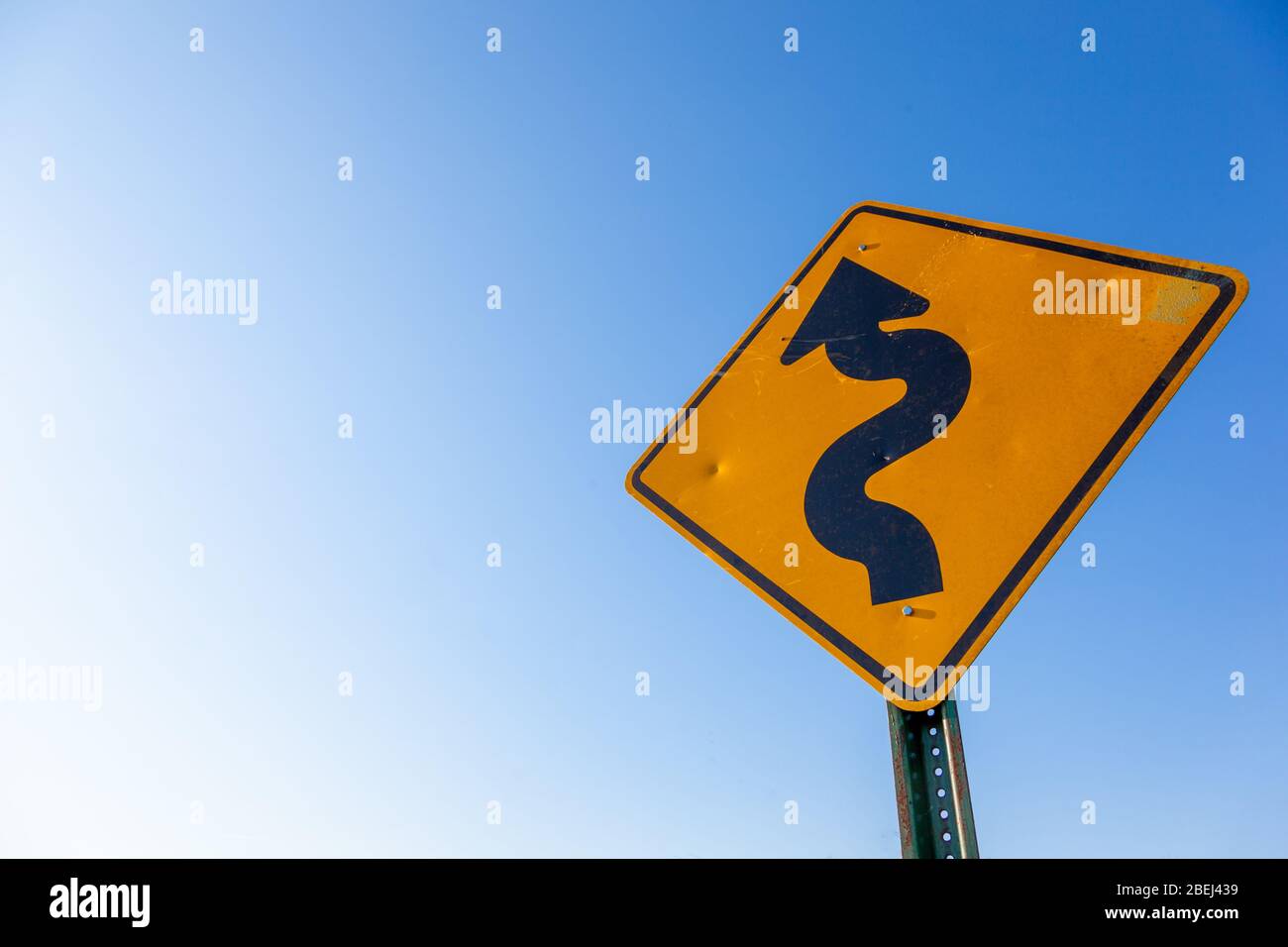 Un panneau incurvé indiquant la prudence routière, ciel bleu avec espace de copie Banque D'Images
