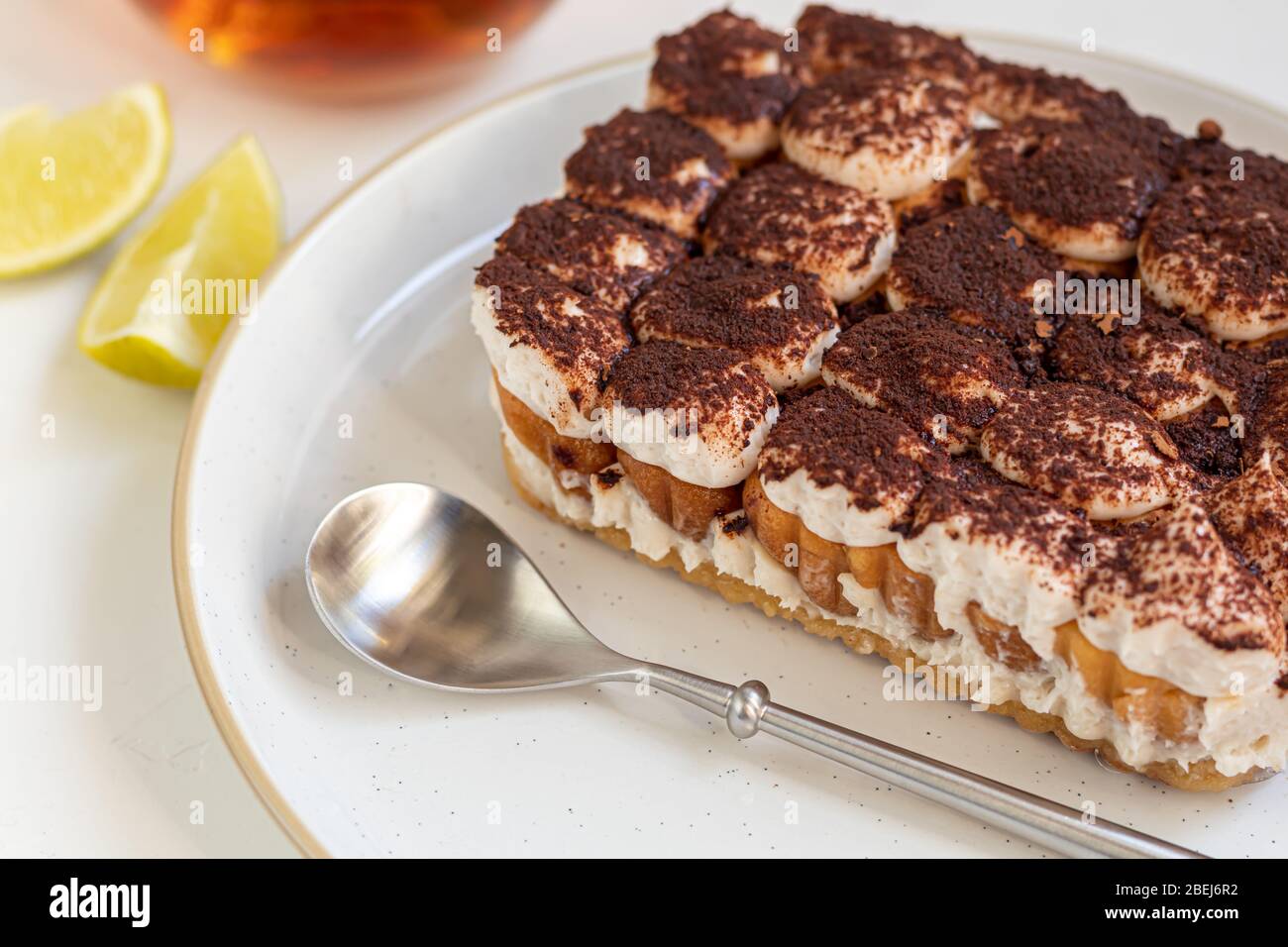 Tiramisu. Dessert italien traditionnel sur fond blanc sous béton. Garnie d'une branche de menthe, de tranches de chaux. Dans une tasse de thé transparente. Banque D'Images