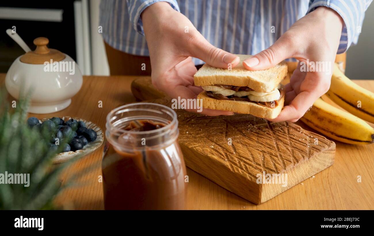 Sandwich au beurre à tartiner au chocolat et à la banane. Les mains féminines tiennent un délicieux petit déjeuner sucré ou un sandwich au déjeuner avec tartiner au chocolat aux noisettes et fres Banque D'Images