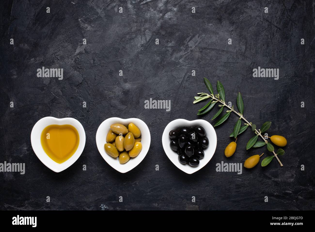 Vue de dessus de la vie avec des bols en céramique, en forme de coeur, avec de l'huile d'olive extra vierge, des olives vertes et noires, sur un fond noir rugueux. Banque D'Images