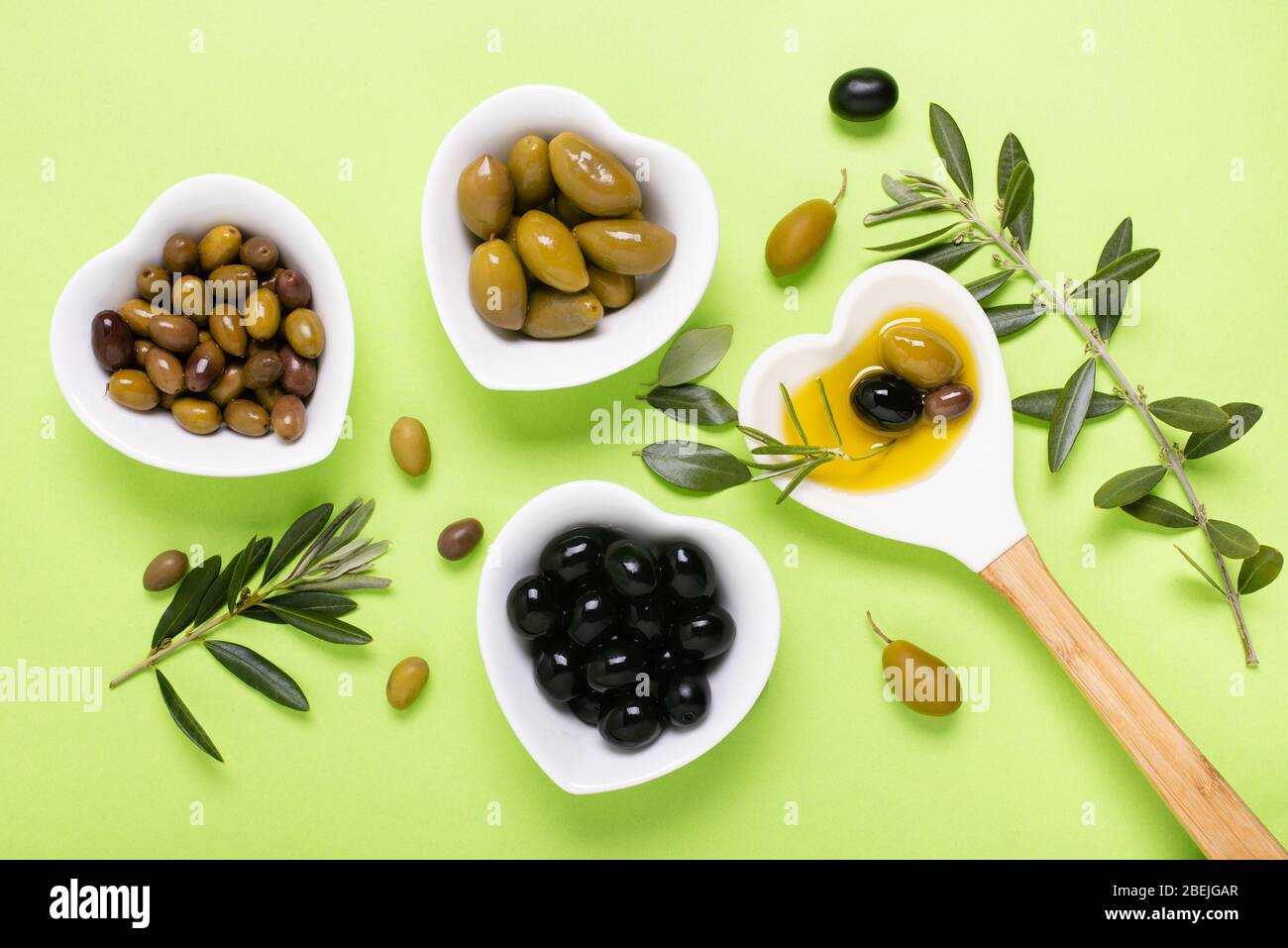 Composition vue d'en haut avec des bols en céramique en forme de coeur, de l'huile d'olive extra vierge, certains types d'olives et de branche d'olive sur un backgrou vert uniforme Banque D'Images