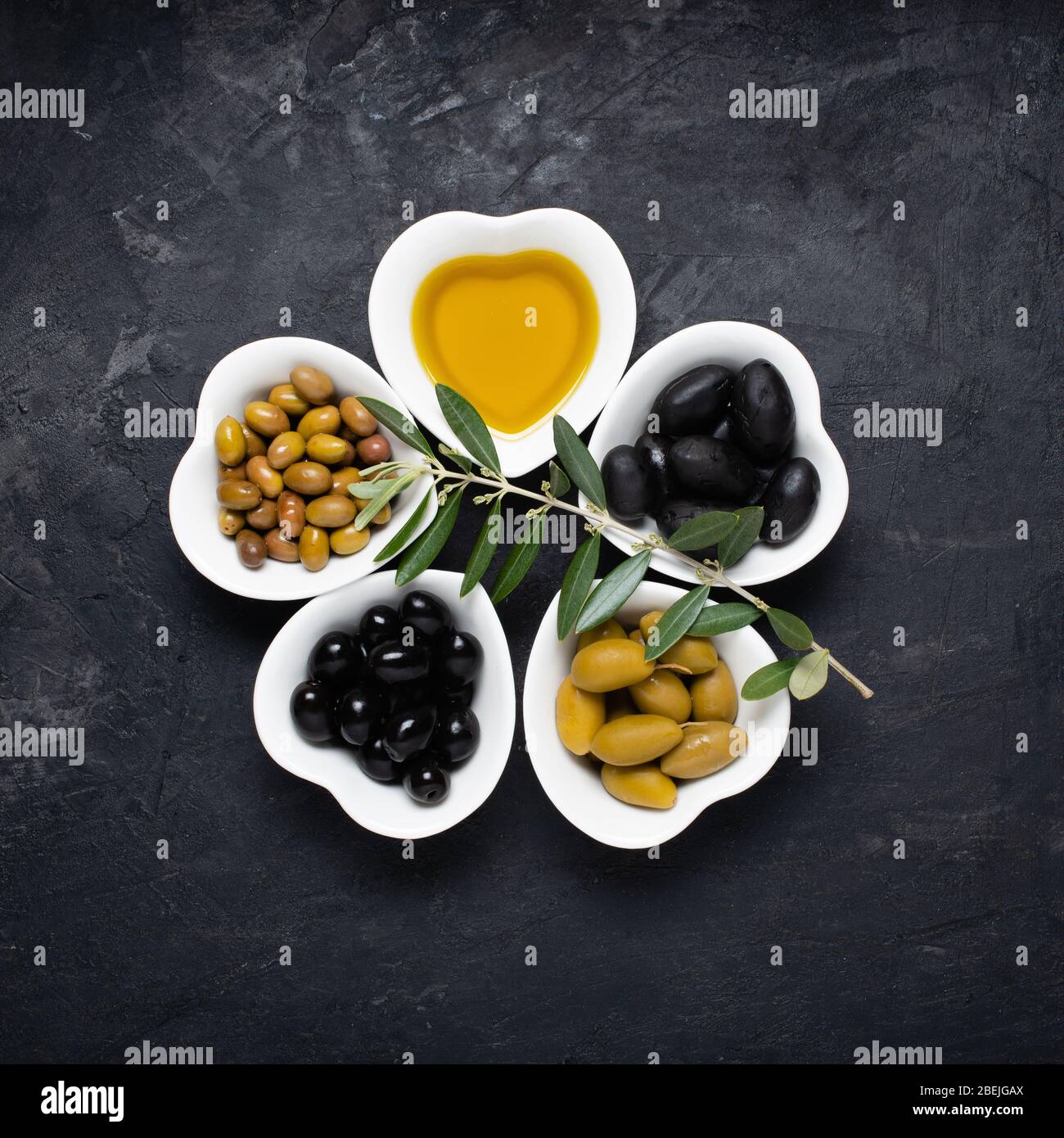 toujours la vie avec des bols en céramique, en forme de coeur, avec de l'huile d'olive extra vierge et différents types d'olives, sur un fond noir rugueux. Haut vi Banque D'Images