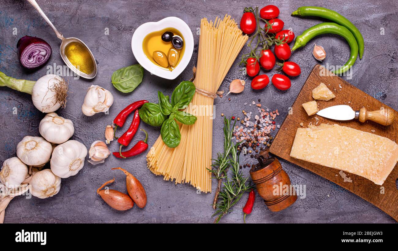 Vue de dessus, sur un fond rustique gris foncé, spaghetti italien avec huile d'olive, fromage assaisonné, bouquet de tomates, divers légumes et épices Banque D'Images