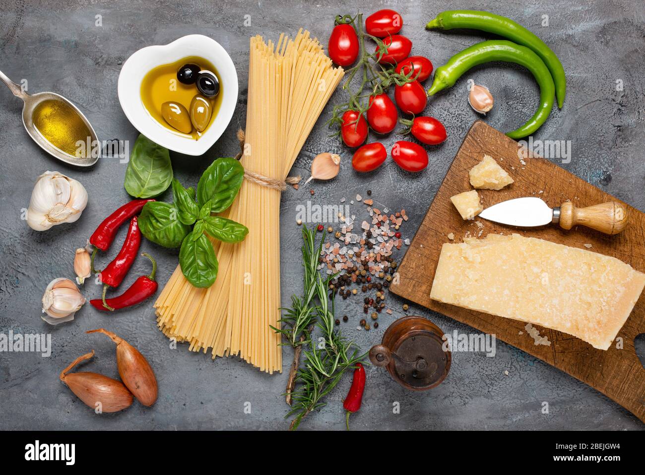 Vue de dessus, sur un fond rustique gris foncé, spaghetti italien avec huile d'olive, fromage assaisonné, bouquet de tomates, divers légumes et épices Banque D'Images