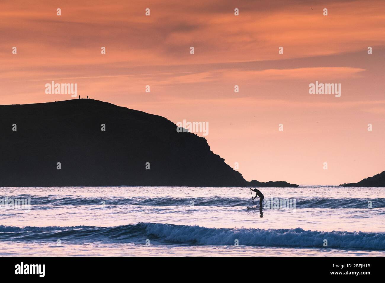 Une paddle-boarder pagayant au-delà de Pentist point East silhouetted par le feu de fin de soirée à Fistral à Newquay, dans Cornwall. Banque D'Images