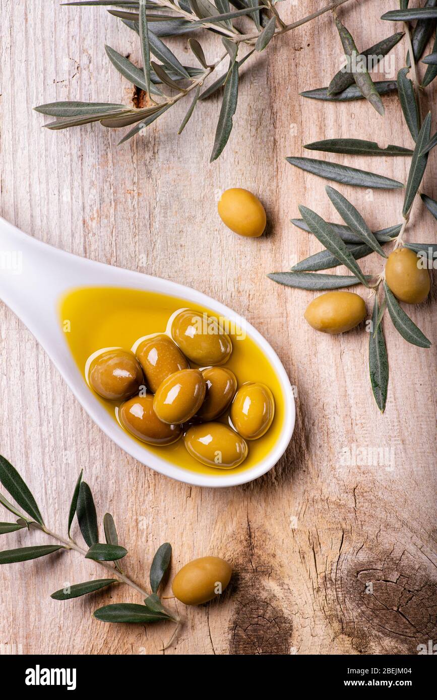 Vue en grand angle, bol en céramique blanc, avec huile d'olive extra vierge et olives vertes, sur table en bois rustique avec branche d'olive Banque D'Images