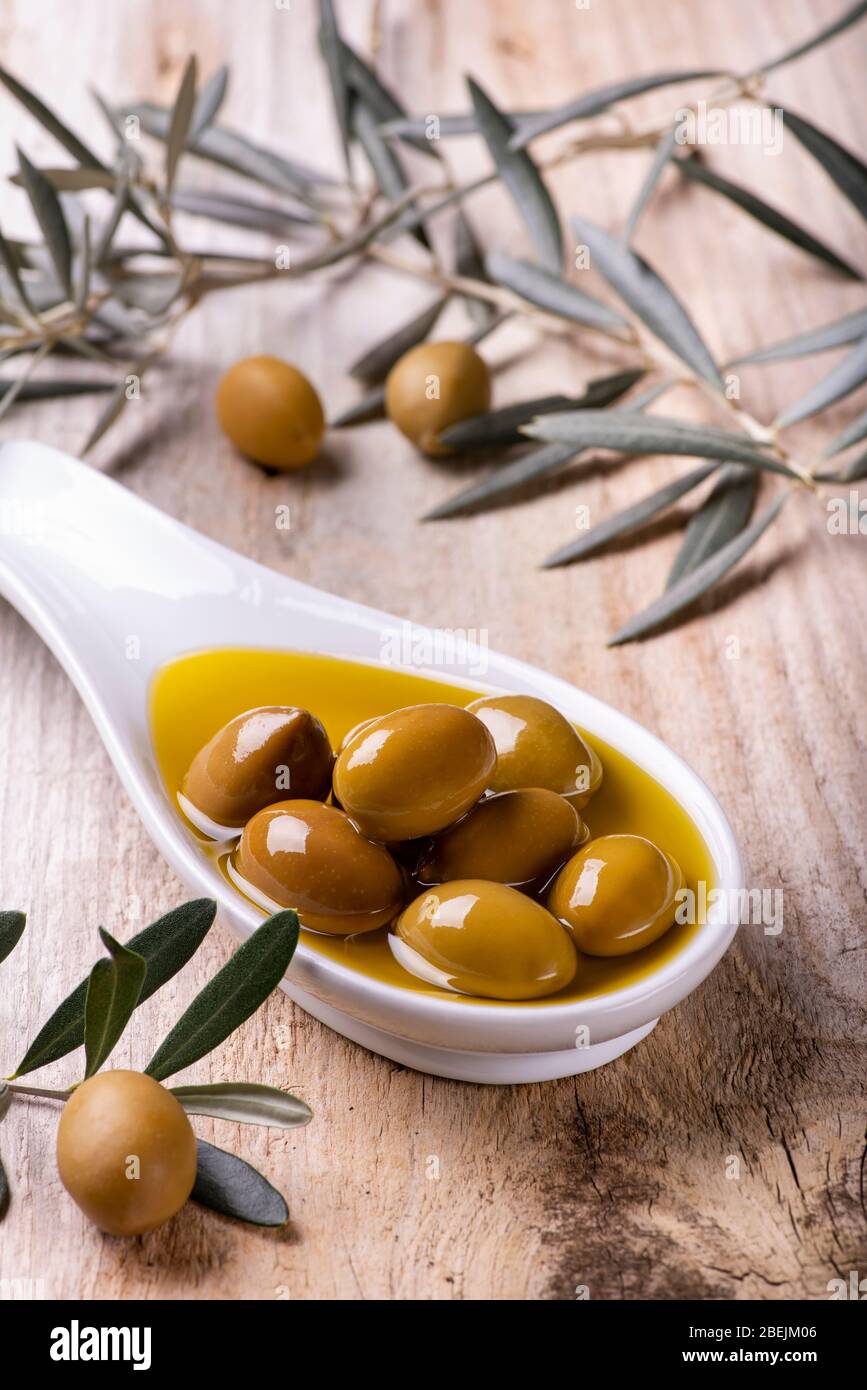 Au premier plan, un bol en céramique blanc, avec de l'huile d'olive extra vierge et des olives vertes, sur la table rustique en bois avec branche d'olive Banque D'Images