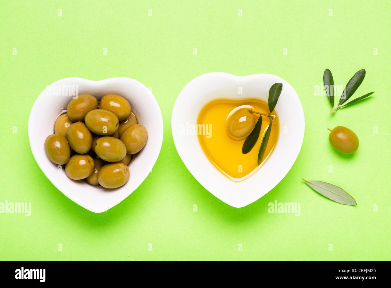 vue de dessus, sur fond vert uniforme, deux bols en céramique blanche en forme de coeur aux olives et à l'huile d'olive extra vierge Banque D'Images