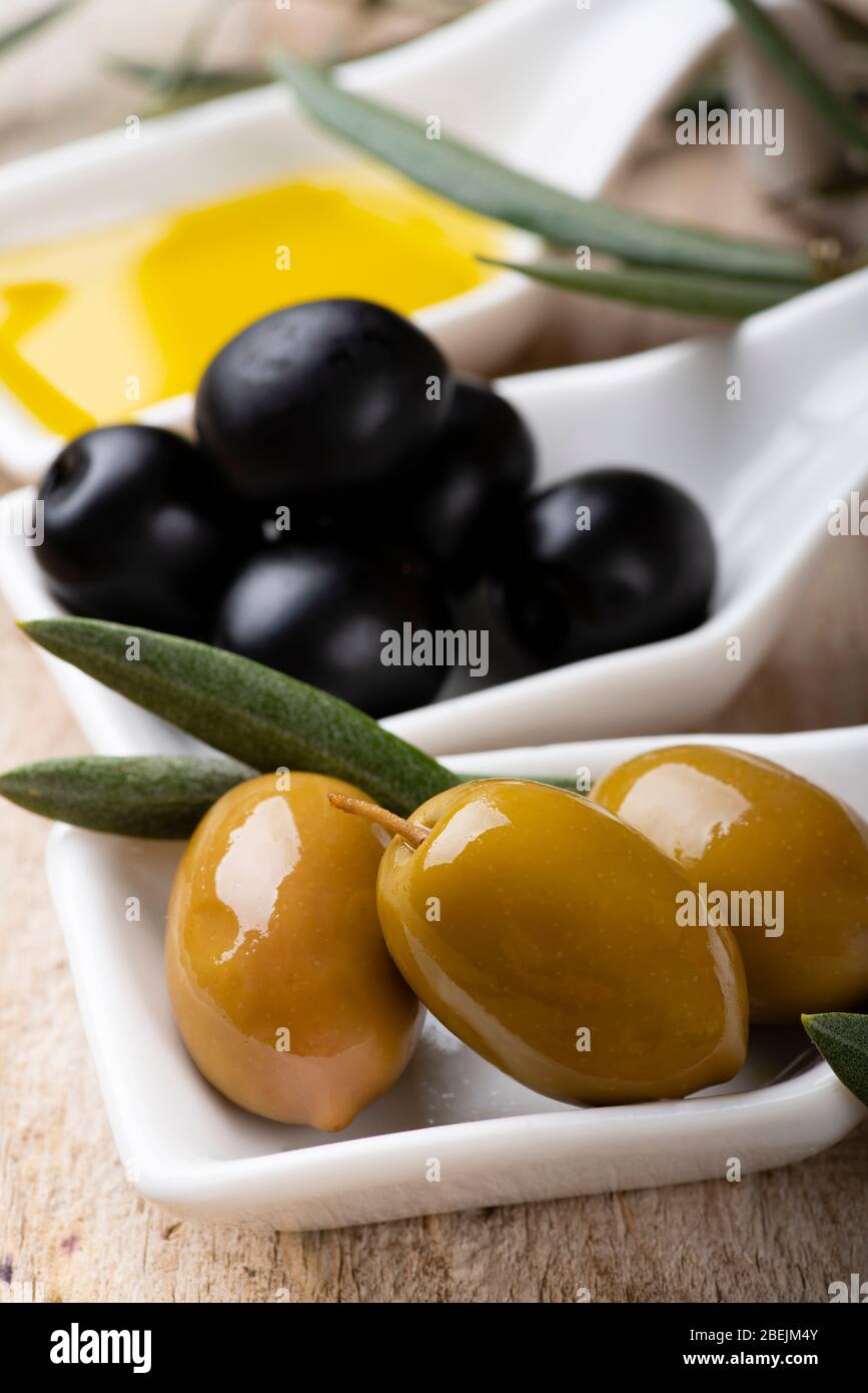 au premier plan, sur la table rustique en bois, quelques bols en céramique blancs avec des olives vertes et noires et de l'huile d'olive extra vierge. Banque D'Images