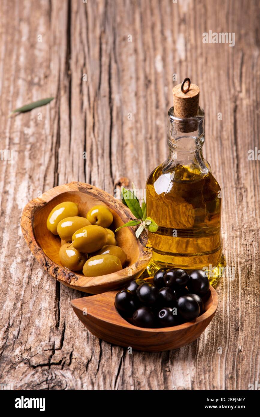au premier plan, sur la table rustique en bois, bols avec olives vertes et noires, branche olive et huile d'olive extra vierge Banque D'Images