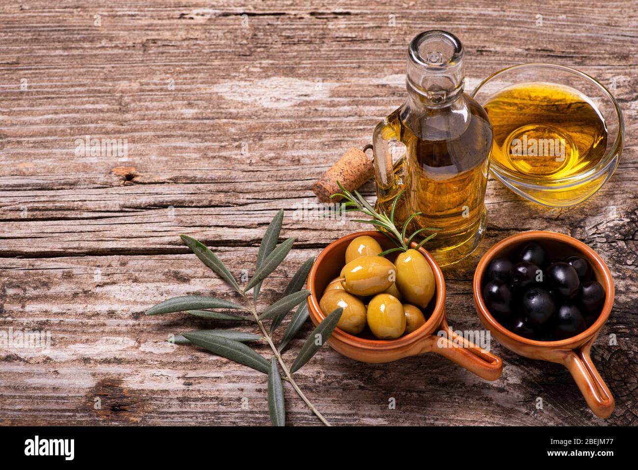 au premier plan, sur la table rustique en bois, bols avec olives vertes et noires, branche olive et huile d'olive extra vierge Banque D'Images