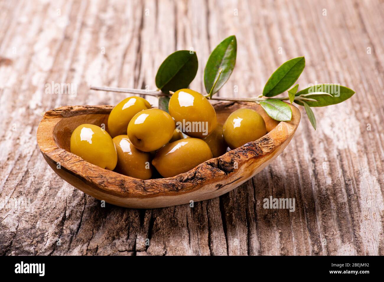 au premier plan, sur la table rustique en bois, un bol en bois aux olives vertes et à la branche olive Banque D'Images