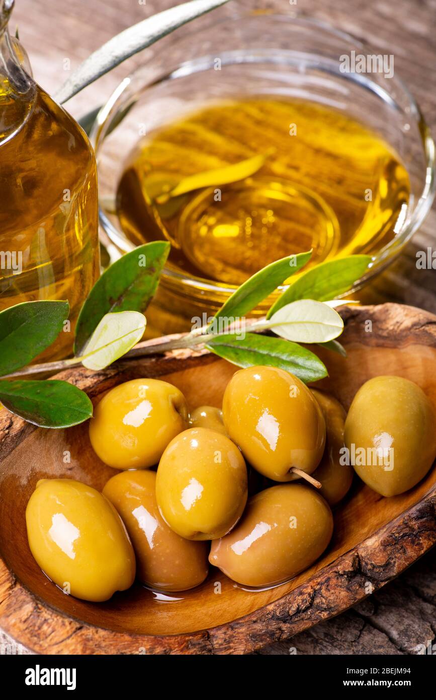 au premier plan, sur la table rustique en bois, un bol en bois aux olives vertes, à la branche olive et à l'huile d'olive extra vierge Banque D'Images