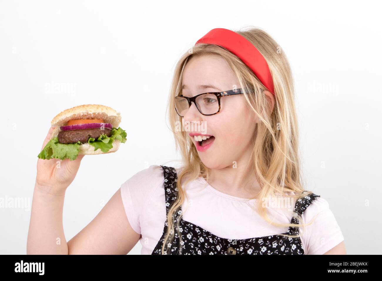 Une jeune fille blonde porte des lunettes dans un groupe rouge Alice qui tient un hamburger maison Banque D'Images