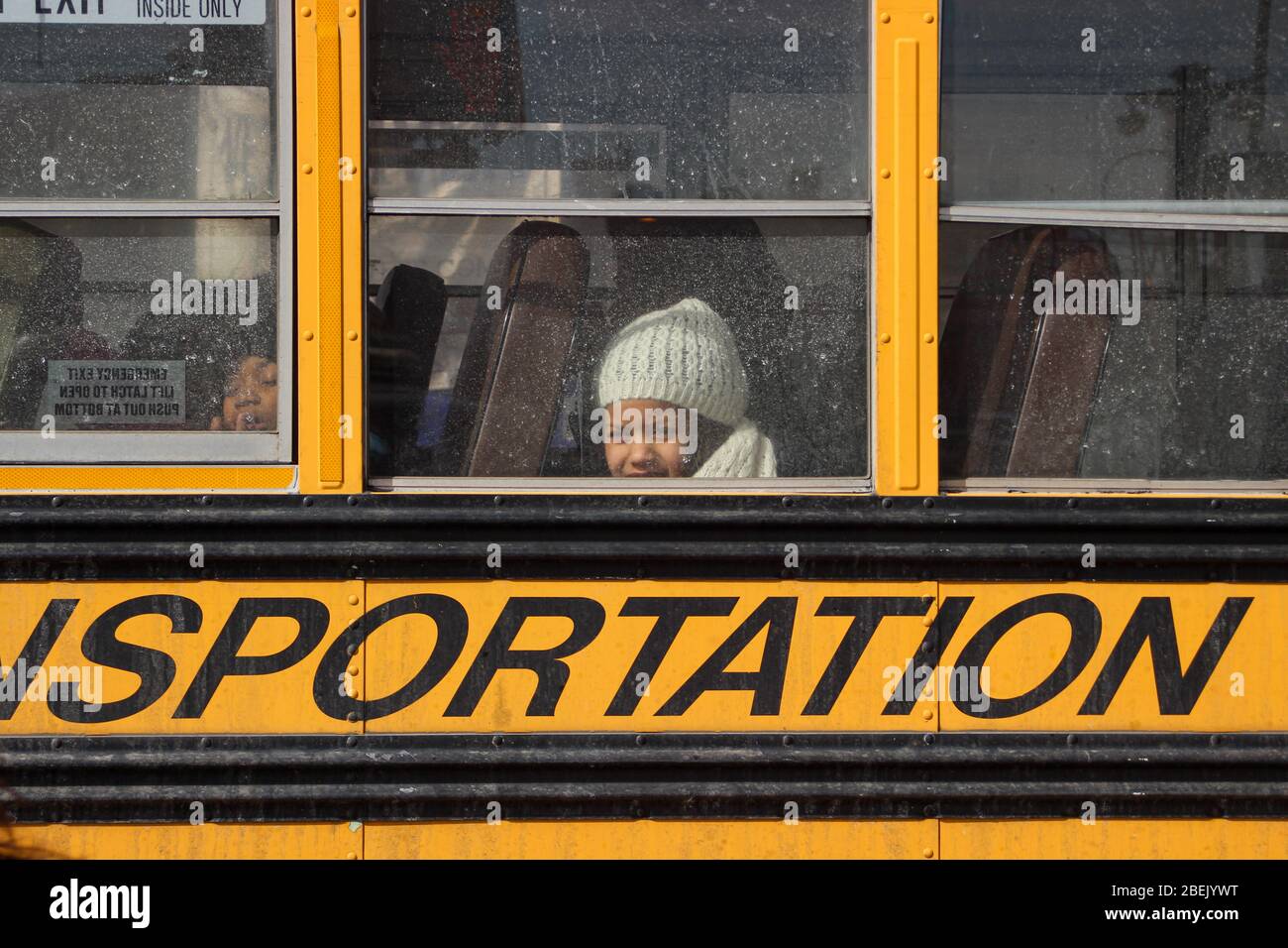 Petite fille avec bonnet blanc regardant la caméra par la sale fenêtre de bus scolaire dans le bas-est, Manhattan, New York City, États-Unis d'Amérique Banque D'Images