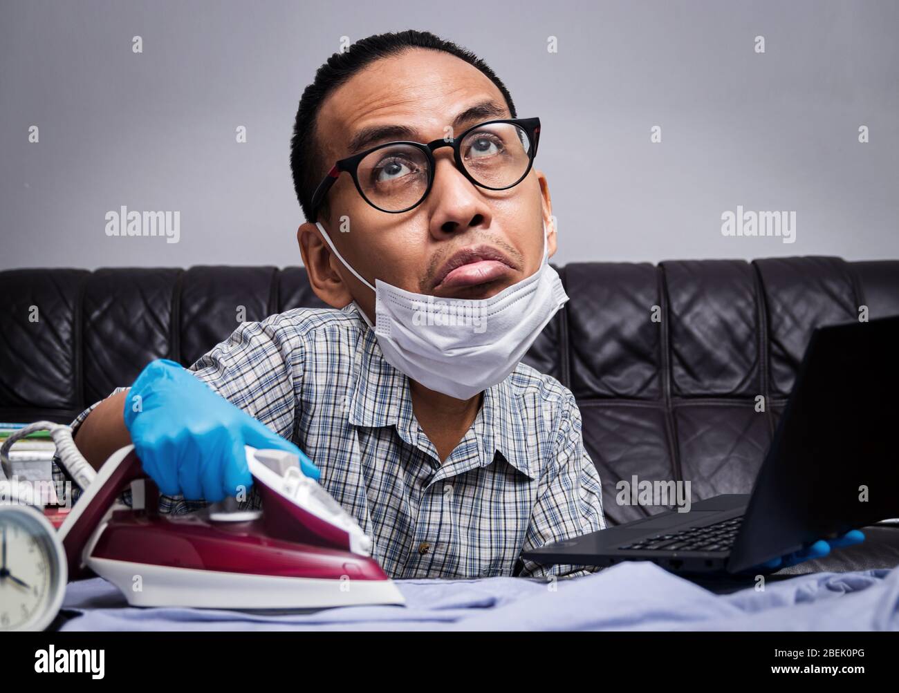 homme avec un visage ennuyeux travaillant avec des pièces très fréquentée pour les affaires et les travaux ménagers, un tissu à repasser et travailler avec un ordinateur portable pendant l'auto-isolation pour éviter la tartiner Banque D'Images