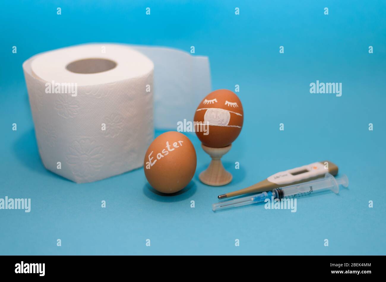 Oeuf de Pâques, papier toilette, thermomètre et seringue sur fond bleu. Coronavirus Covid-19. Photo concept. Pâques 2020. Banque D'Images