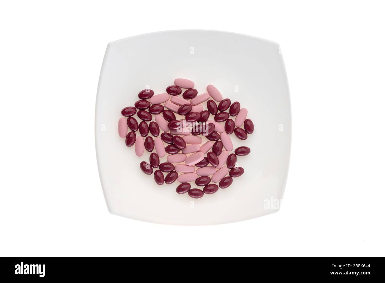 Une pile de pilules sur une plaque blanche symbolisant la nourriture. Vitamines sur fond blanc isolé. Pilules roses et gels bordeaux. Repas de prescription Banque D'Images