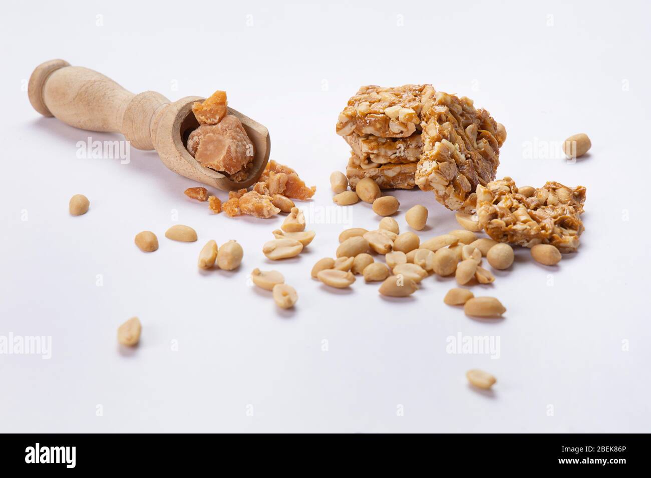 La quincaillerie dans une cuillère en bois gardée avec mungfali chikki et des arachides sur fond blanc. Banque D'Images