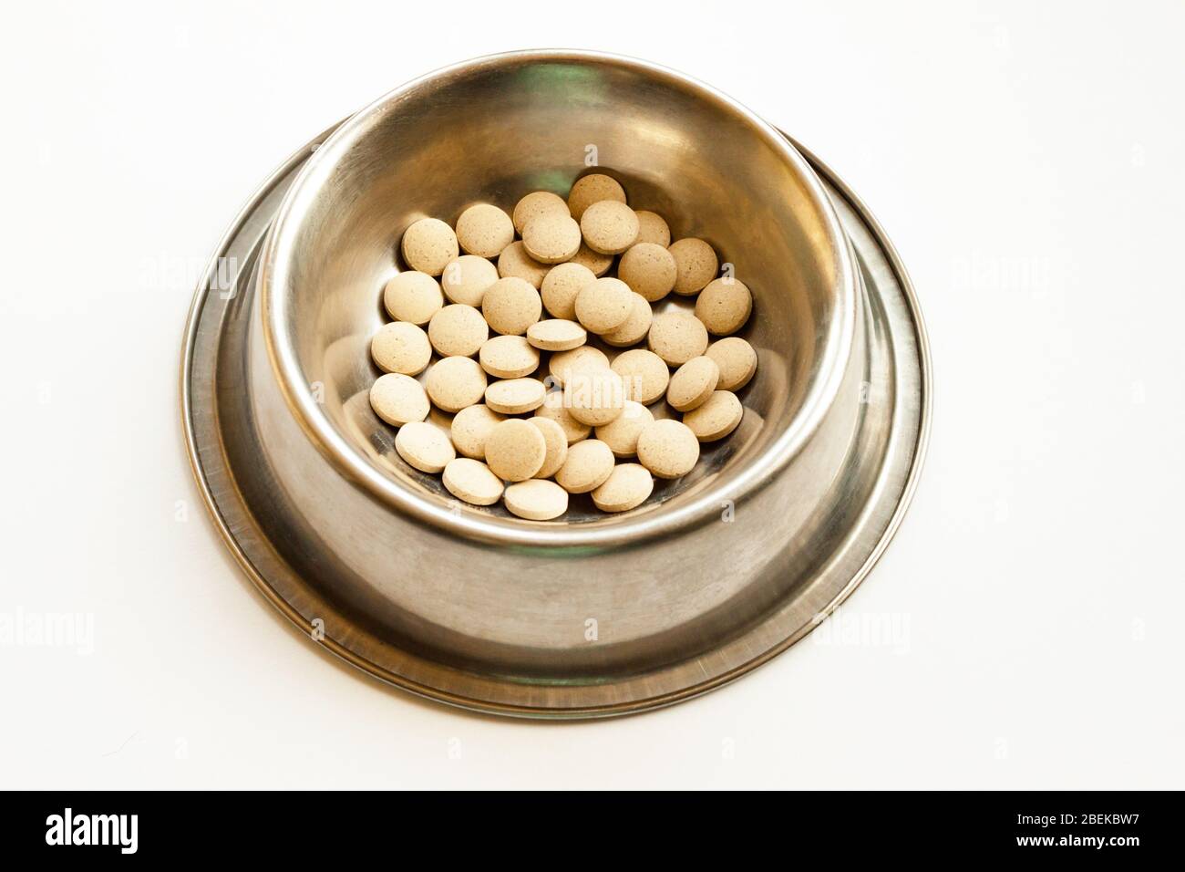 Comprimés de suppléments de vitamines pour chats et chiens dans un bol en métal sur fond blanc. Concept de santé PET Banque D'Images