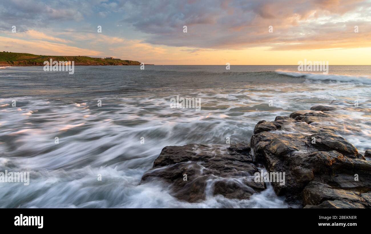 Vue sur le lever du soleil sur la plage de Cocklawburn à marée haute avec mouvement de vague et un ciel spectaculaire ajoutant de la texture à la scène sur la côte de Northumberland. Banque D'Images