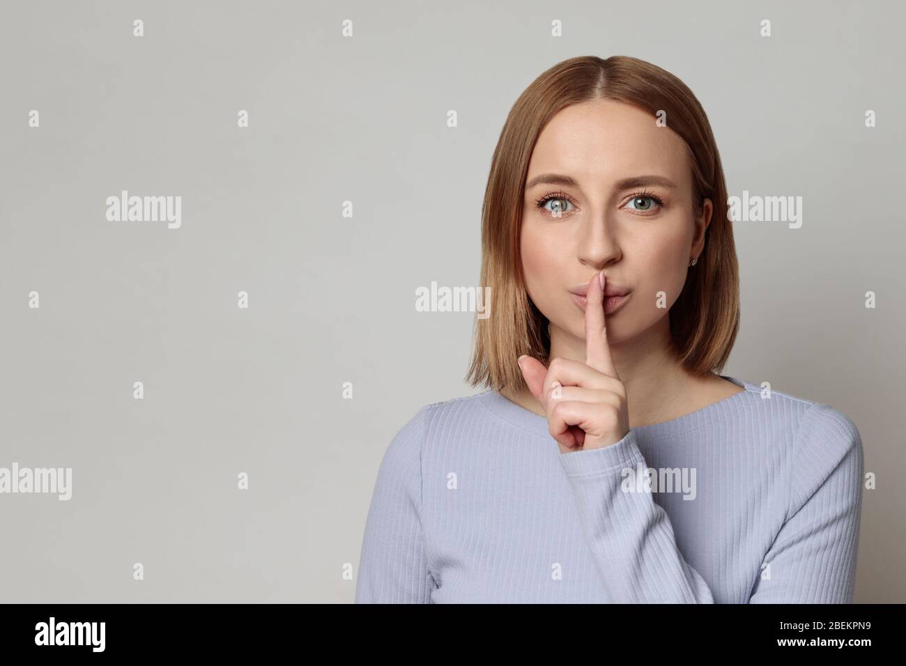 Shhh ! Une mystérieuse femme européenne avec des cheveux courts garde l'index sur les lèvres gestuelle du silence, isolée sur fond gris avec espace de copie. Gardez qui Banque D'Images