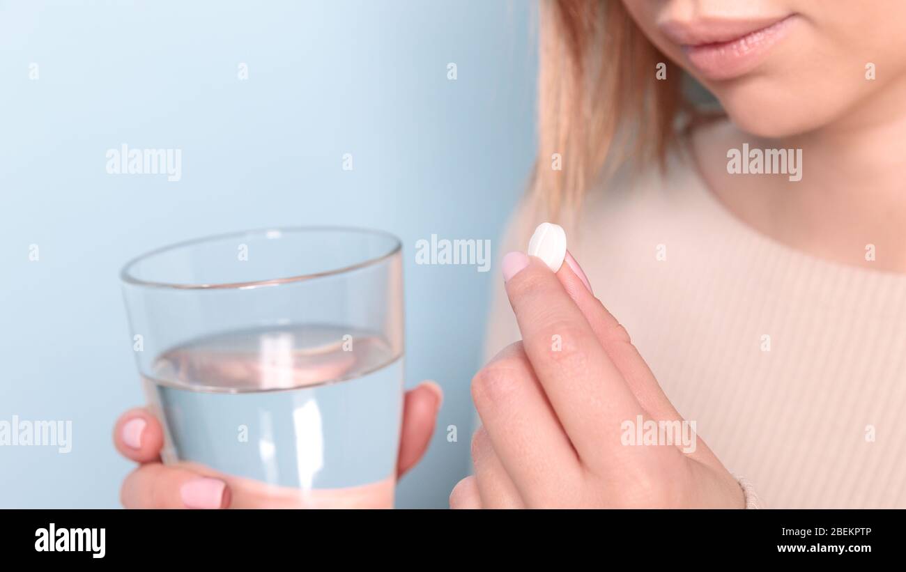 Gros plan sur une jeune femme malsaine prenant en pilule et un verre d'eau. Fond bleu. Banque D'Images