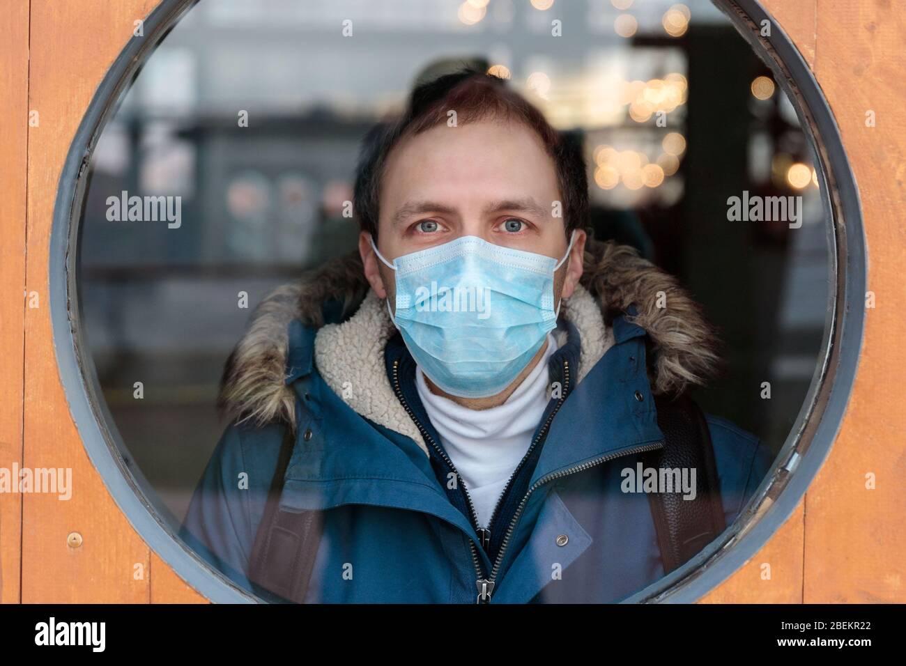 L'homme regarde la fenêtre ronde, porte un masque médical de protection contre les maladies infectieuses transmissibles et comme protection contre la grippe ou le coronavirus, Banque D'Images