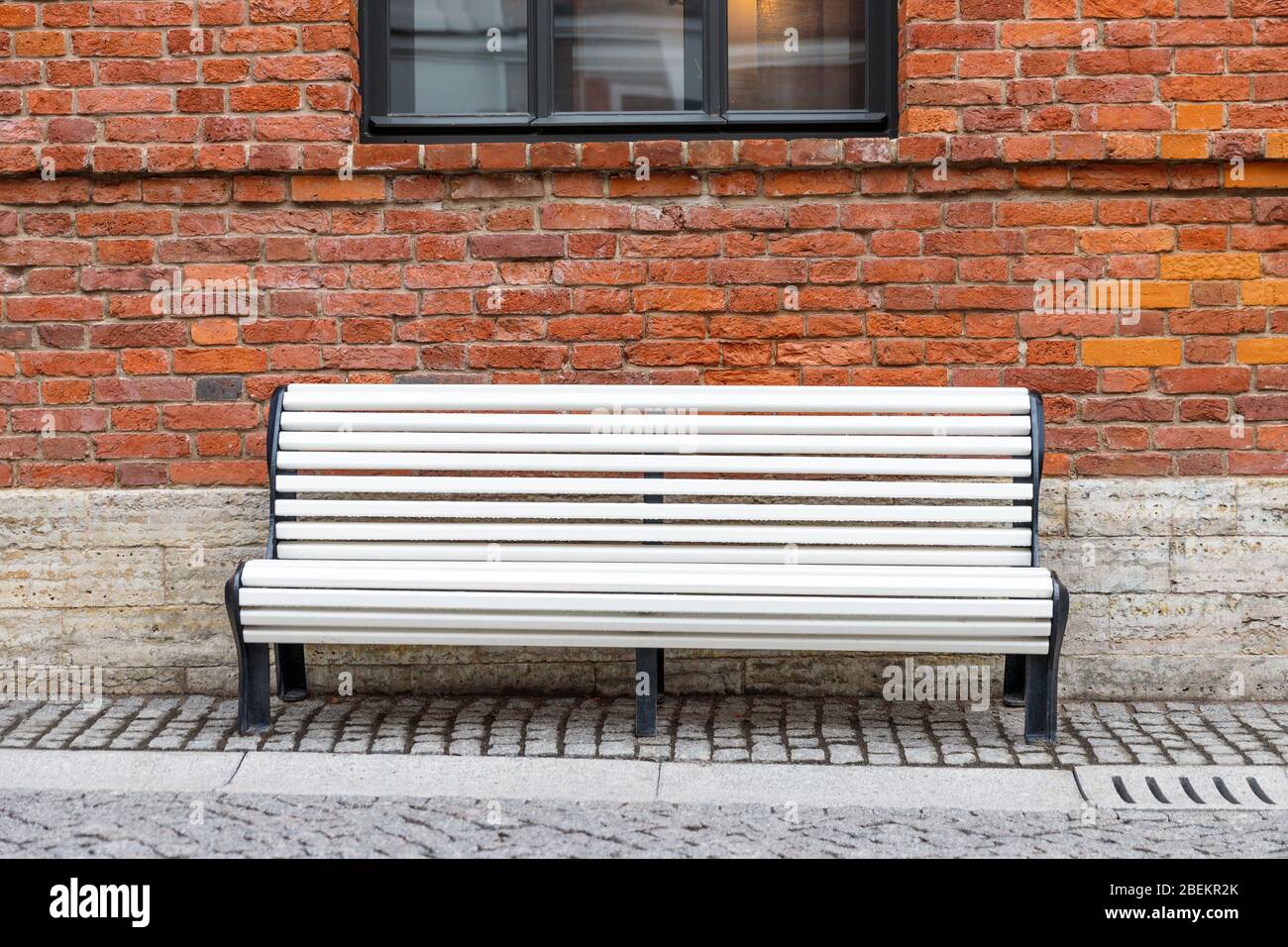 Banc de bois blanc vide solitaire avec vieux mur de brique brun et fenêtre noire sur fond. Banque D'Images