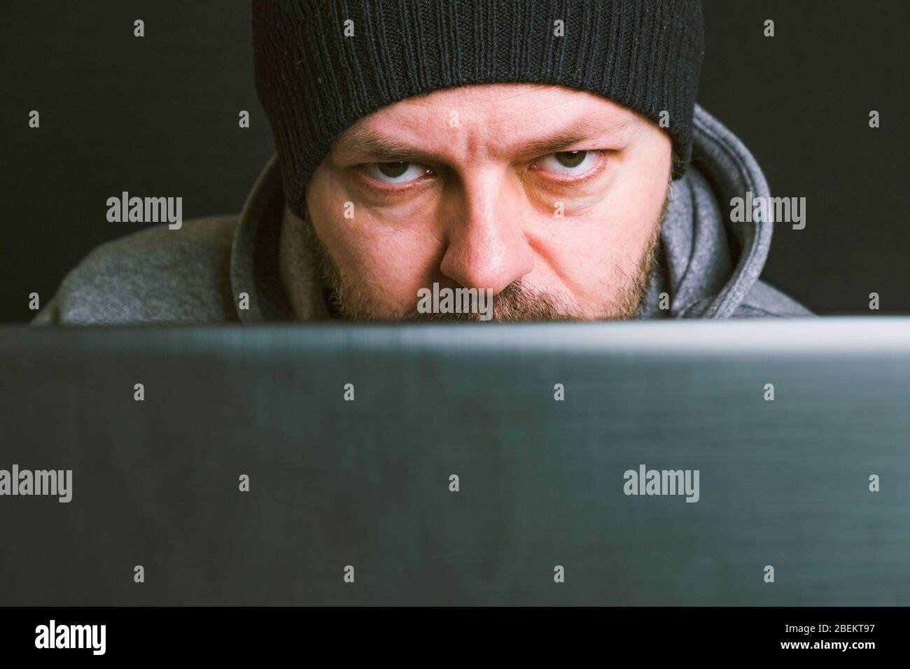 Homme portant un capuchon noir et un sweat à capuche assis derrière le moniteur de l'ordinateur dans le concept sombre, gros plan, pirater le système informatique Banque D'Images