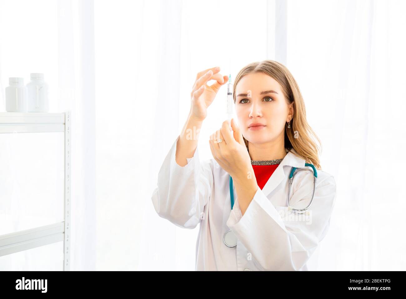 La femme médecin prépare la seringue pour l'injection du patient dans la salle d'examen, toile de fond de rideaux blancs dans l'hôpital ou la clinique. Banque D'Images