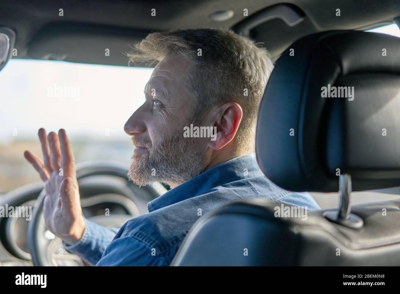 Profil d'un chauffeur de voiture sympathique avec des cheveux et des barbe grisants pris de l'intérieur de la voiture Banque D'Images