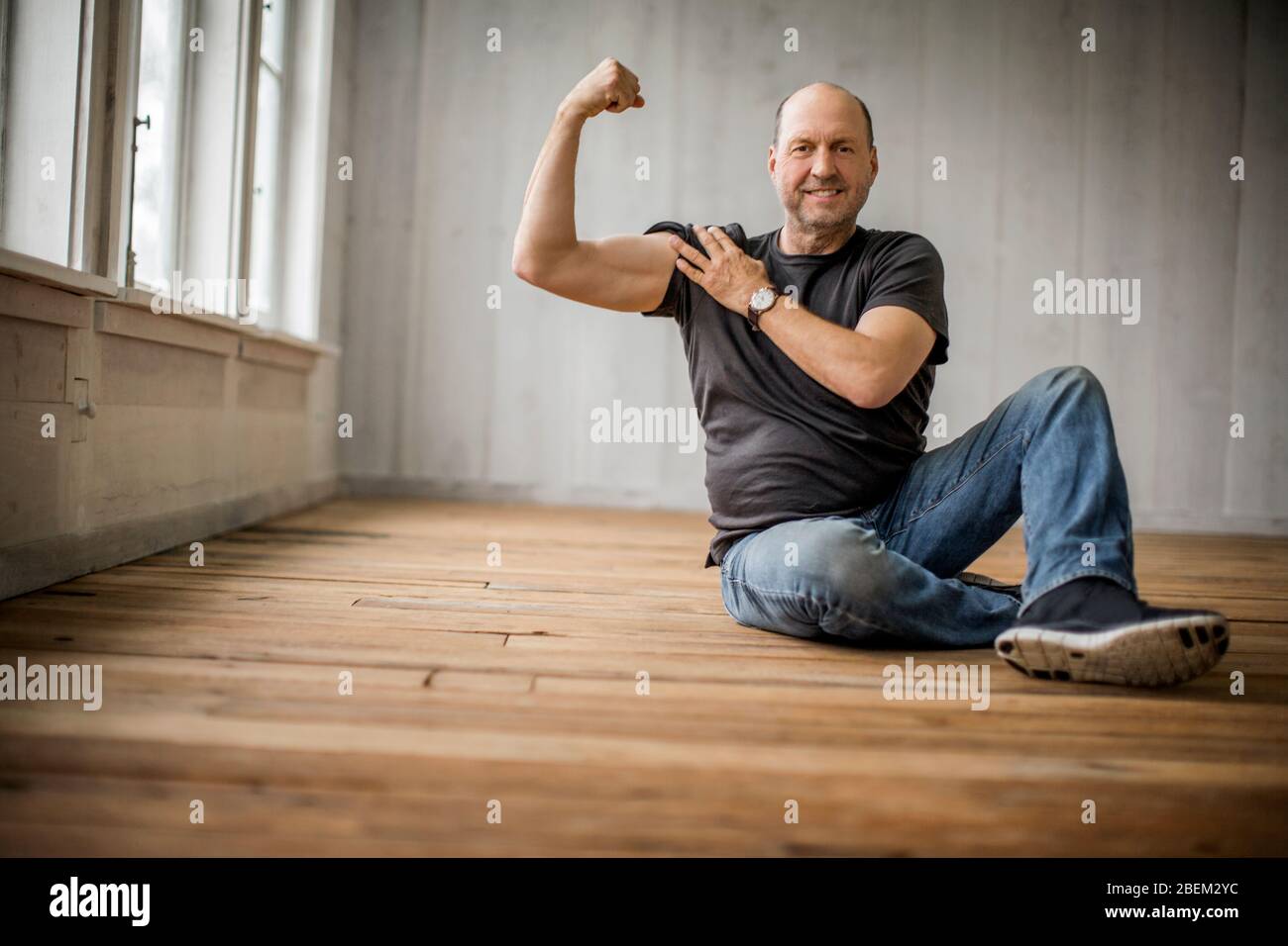 Homme souriant d'âge moyen assis sur le sol fléchit ses muscles Banque D'Images