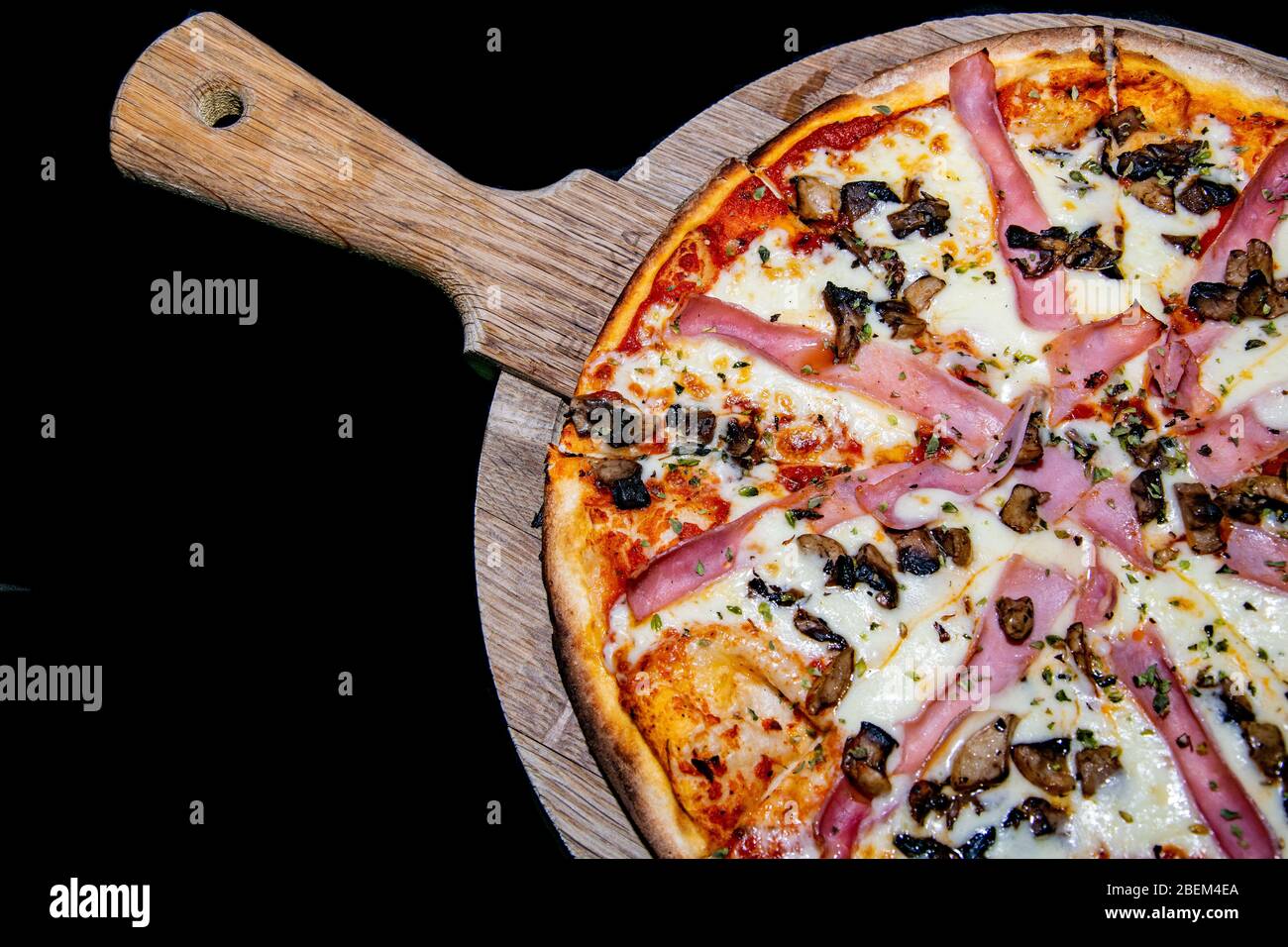 une vue rapprochée d'une pizza aux champignons et au jambon fraîchement cuit servie sur une plaque en bois Banque D'Images