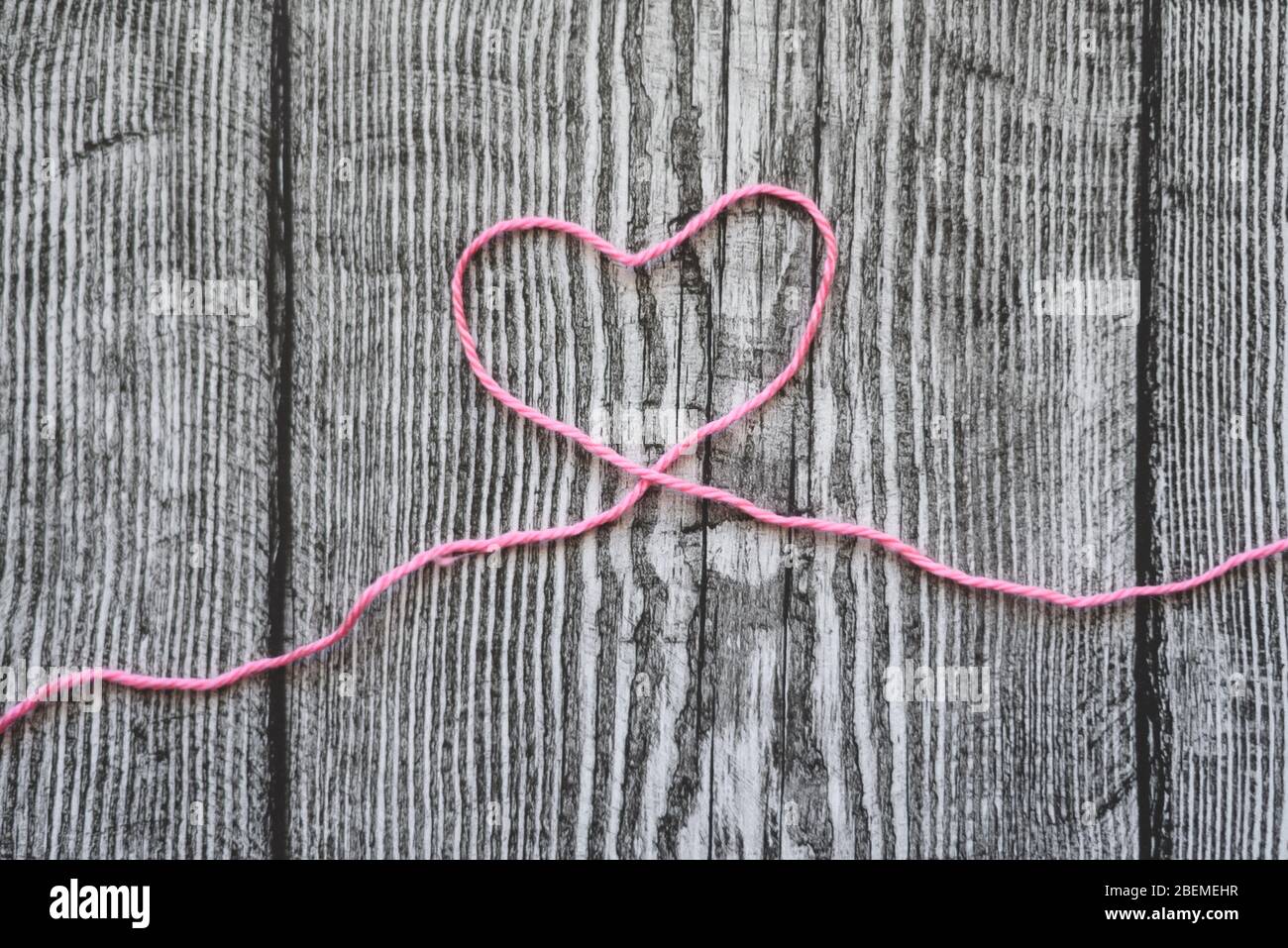 Un coeur en laine rose sur fond gris en bois. Banque D'Images