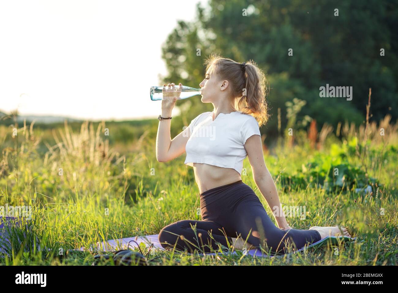 Une fille sportive boit de l'eau lors d'un entraînement. Le concept de sport, d'été et de mode de vie sain. Banque D'Images