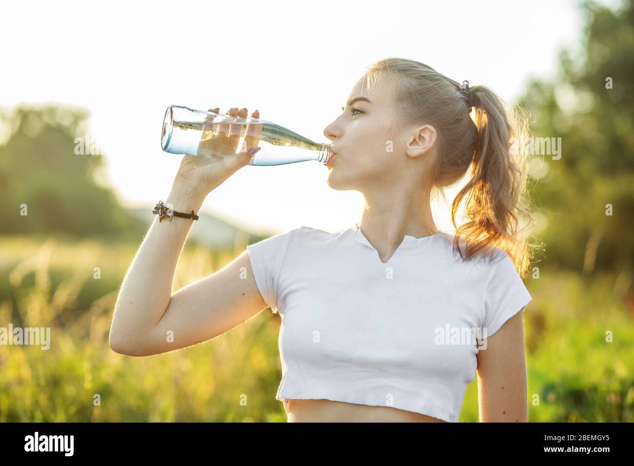 Une fille sportive boit de l'eau après un entraînement. Le concept de sport, d'été et de mode de vie sain. Banque D'Images