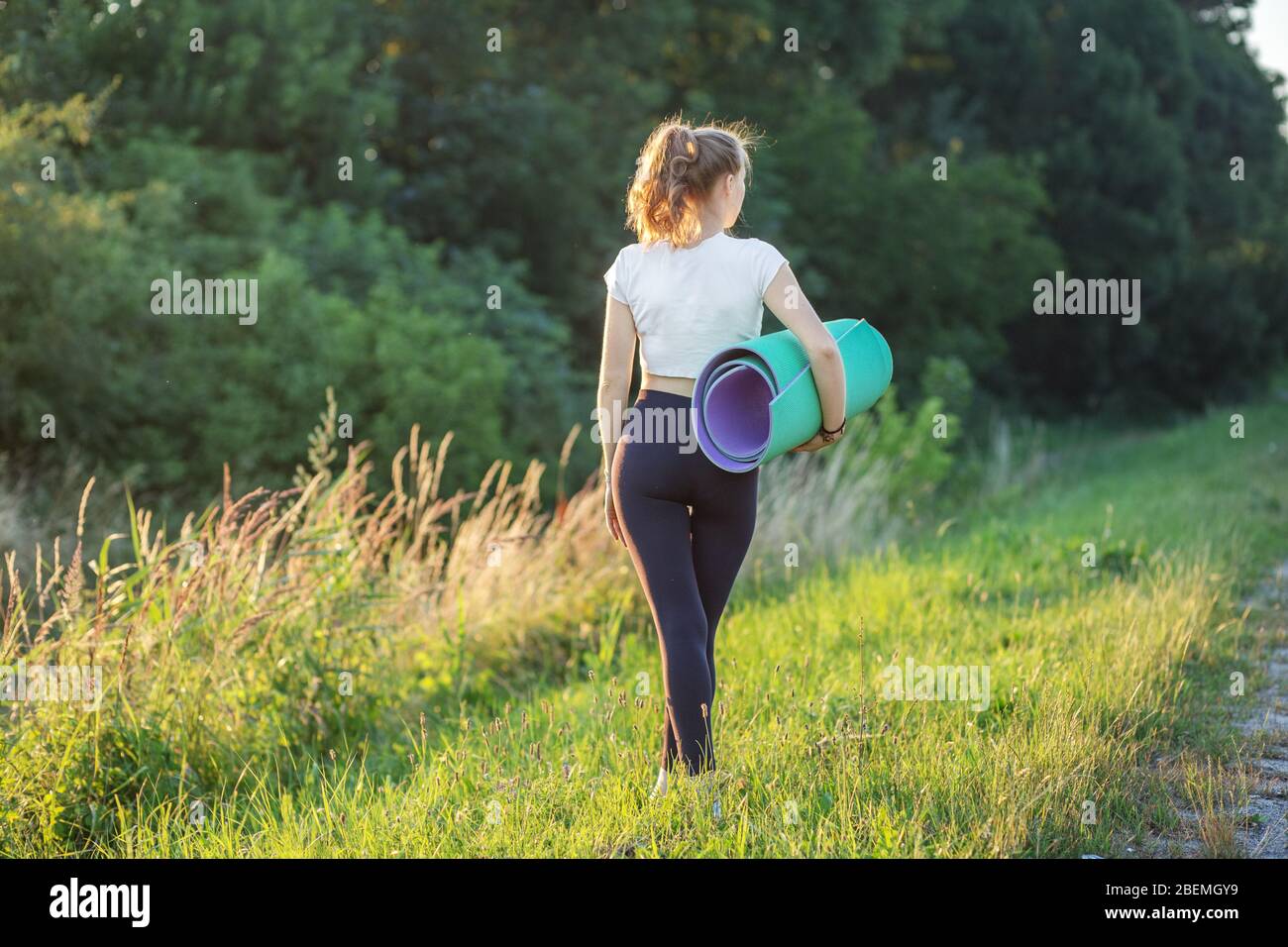 Une fille athlétique porte un tapis pour l'entraînement. Le concept de sport, d'été et de mode de vie sain. Banque D'Images
