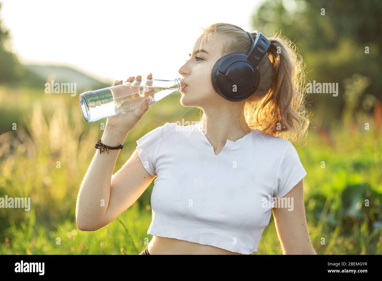 Une fille sportive boit de l'eau. Adolescent dans le casque. Le concept de sport, d'été et de mode de vie sain. Banque D'Images